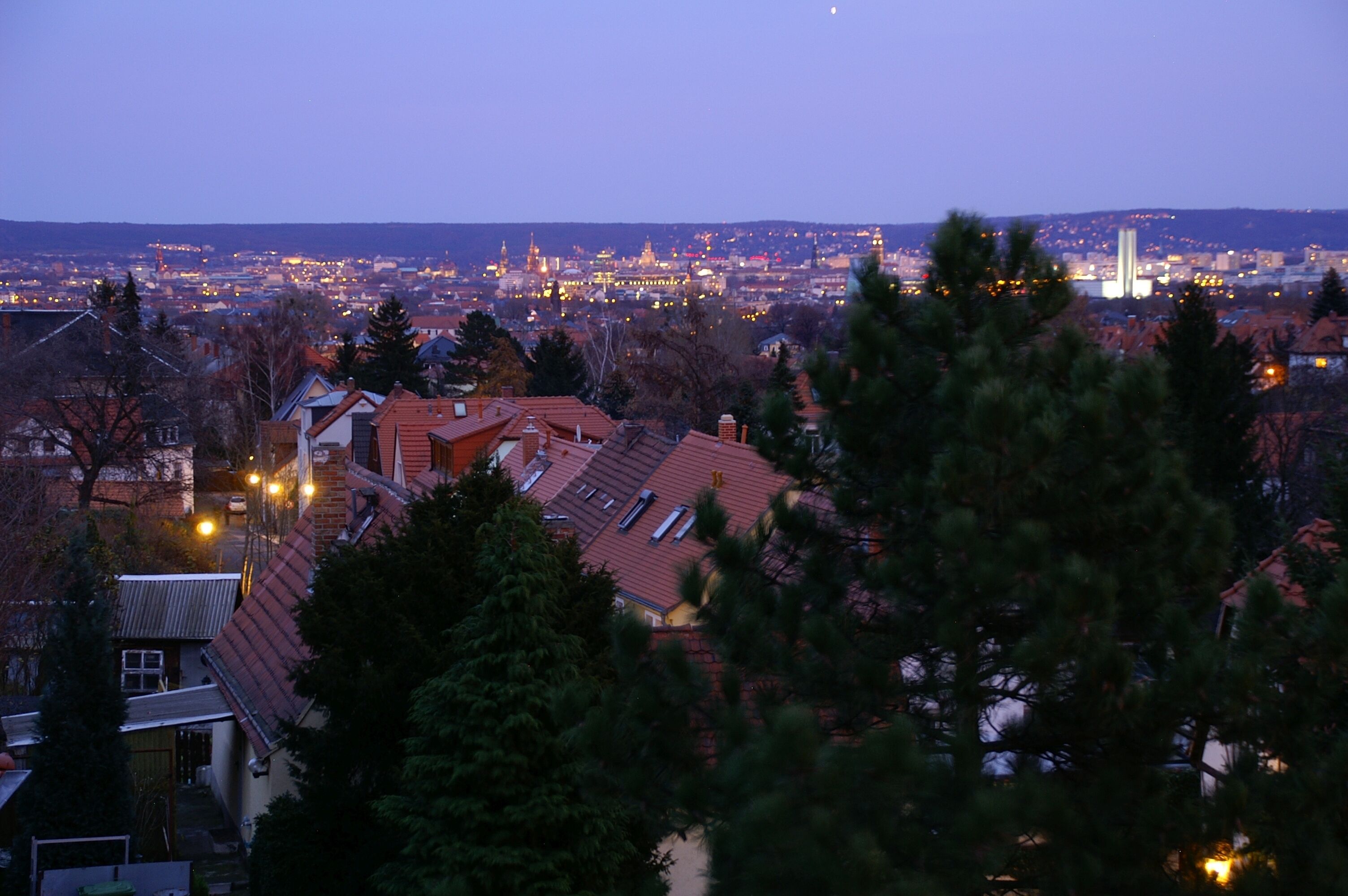 A cityscape at dusk with residential buildings and a distant illuminated skyline.