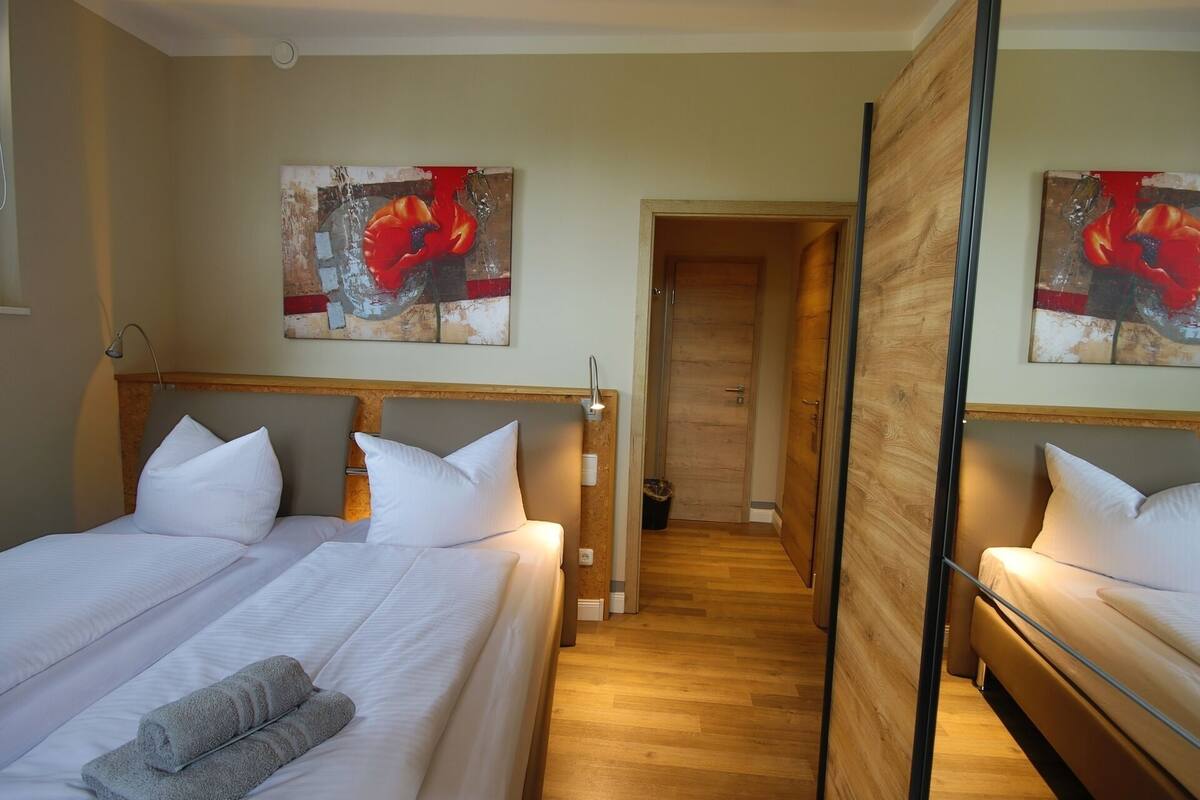 A hotel room with two beds, a wooden floor, and artwork on the walls.
