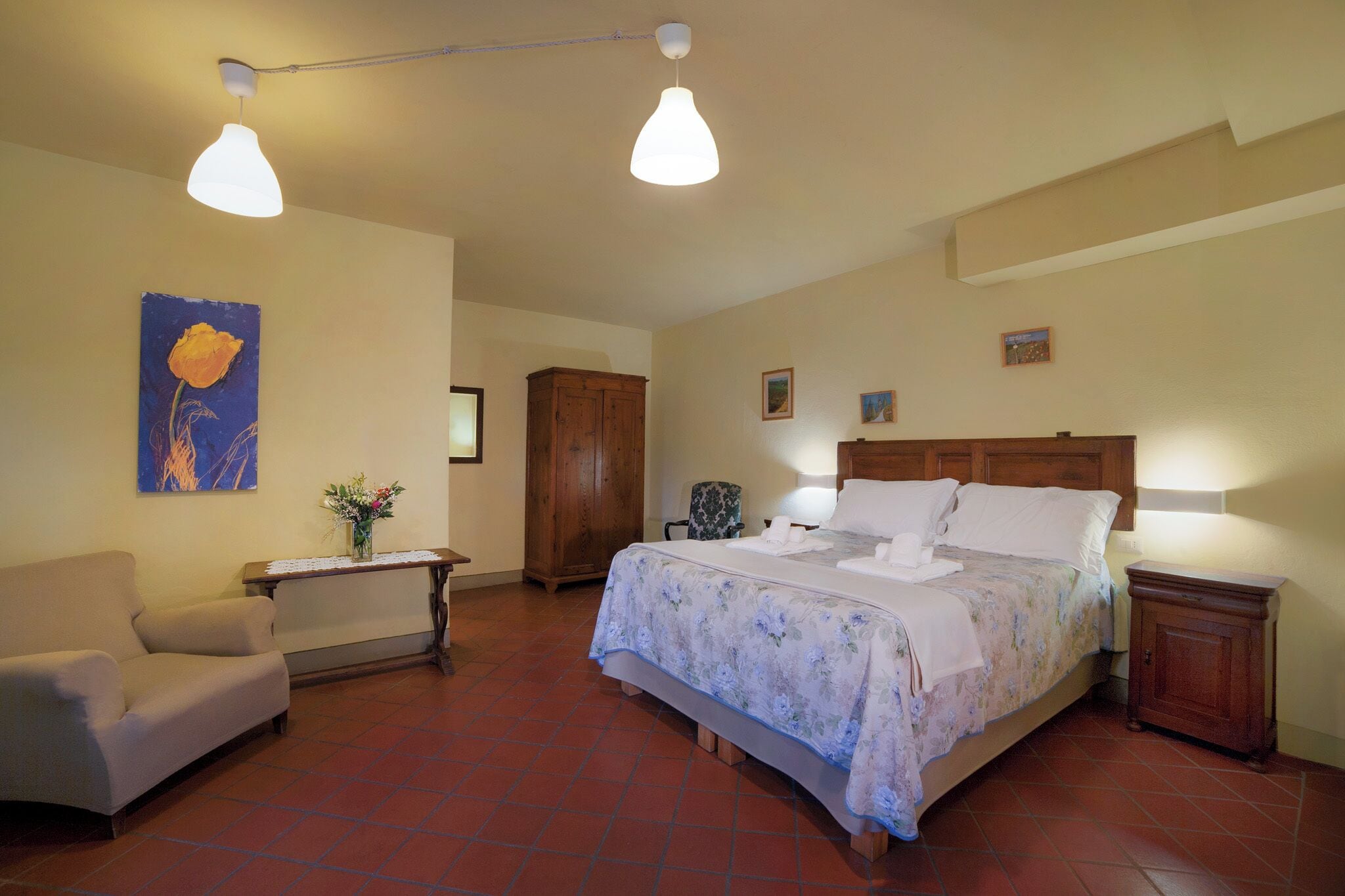 Ein Schlafzimmer mit einem Bett, einem Sessel, einem Holzkasten und einem Bild an der Wand.