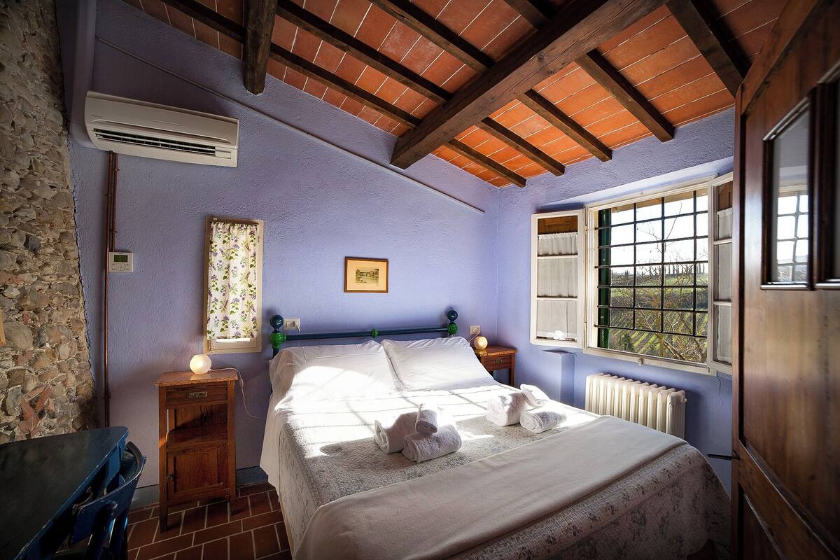 A bedroom with a bed, a window, a radiator, and a stone wall.