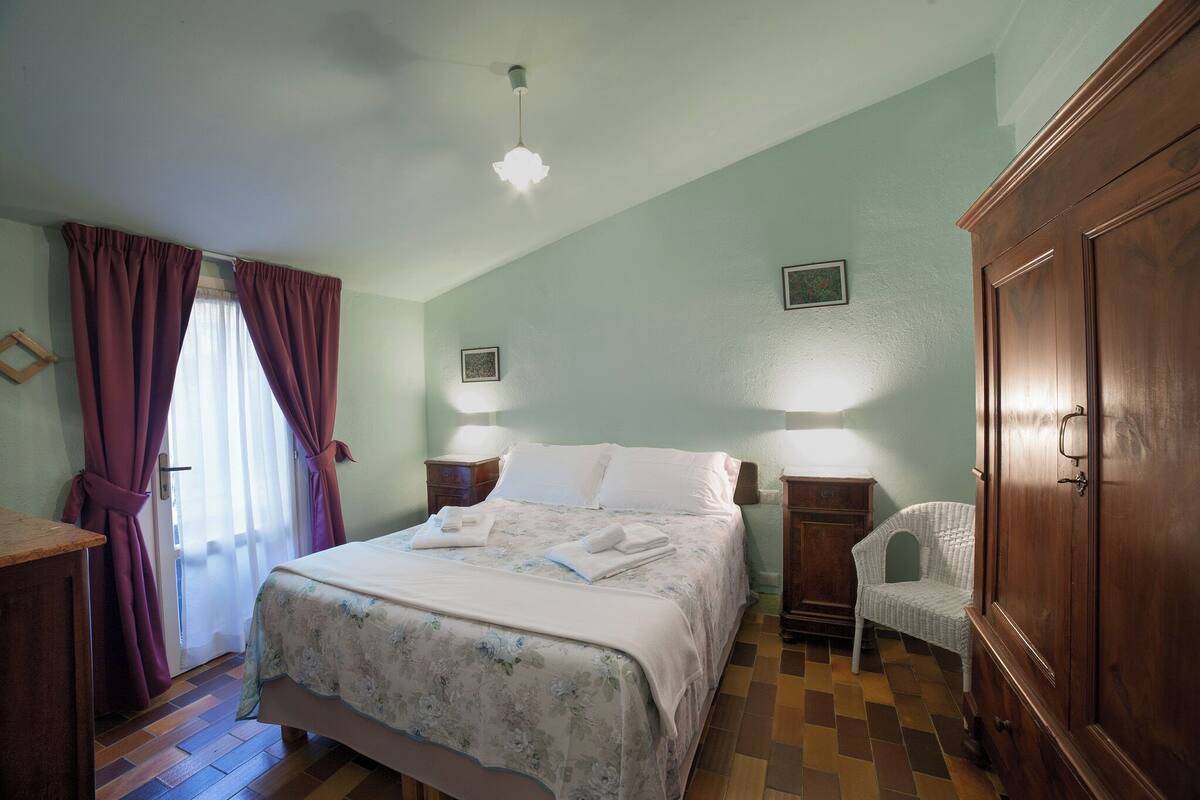 A bedroom with a bed, two bedside tables, a wardrobe, a chair, and a window with curtains.
