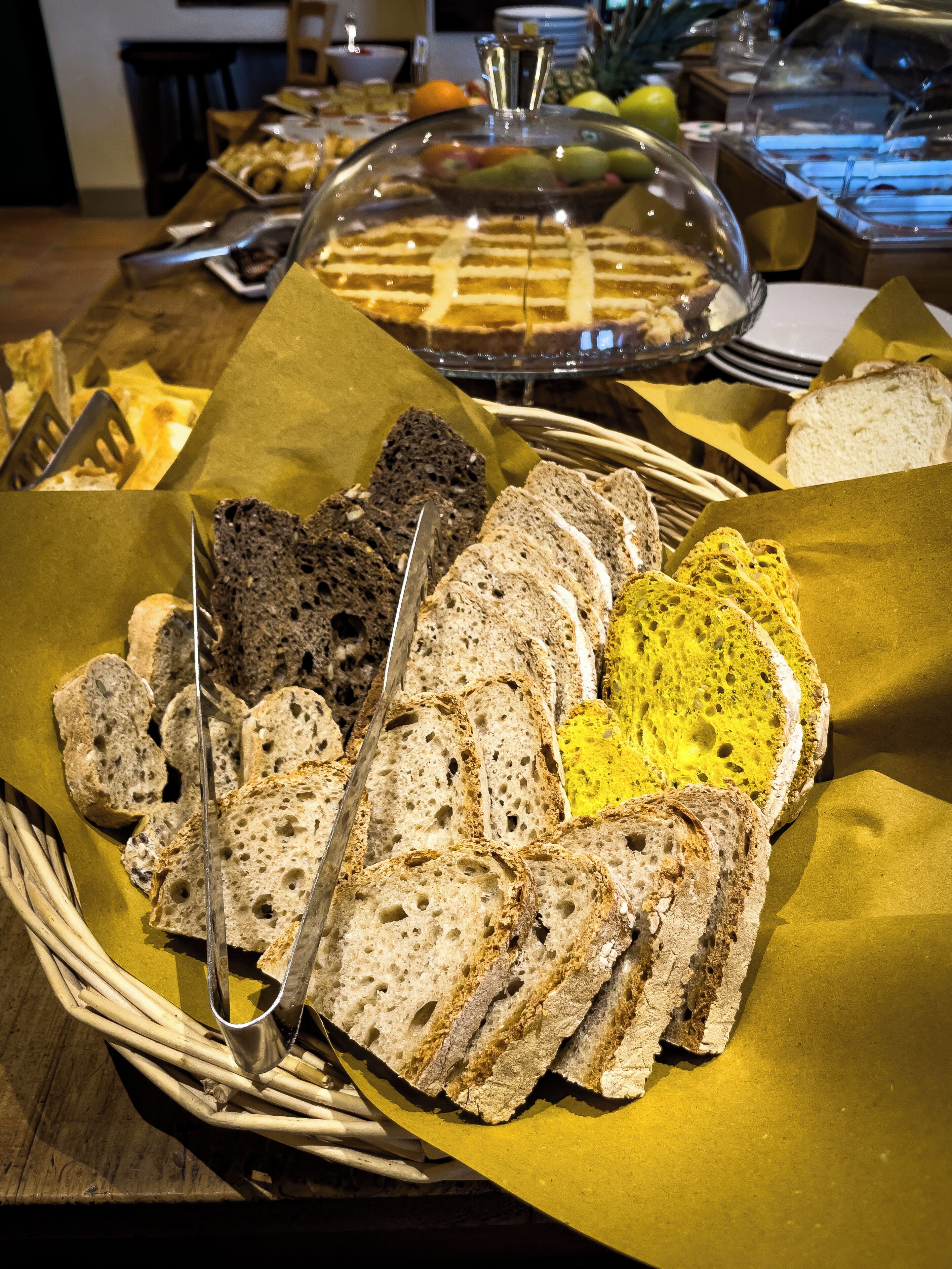 A buffet table with various breads and a covered dessert.