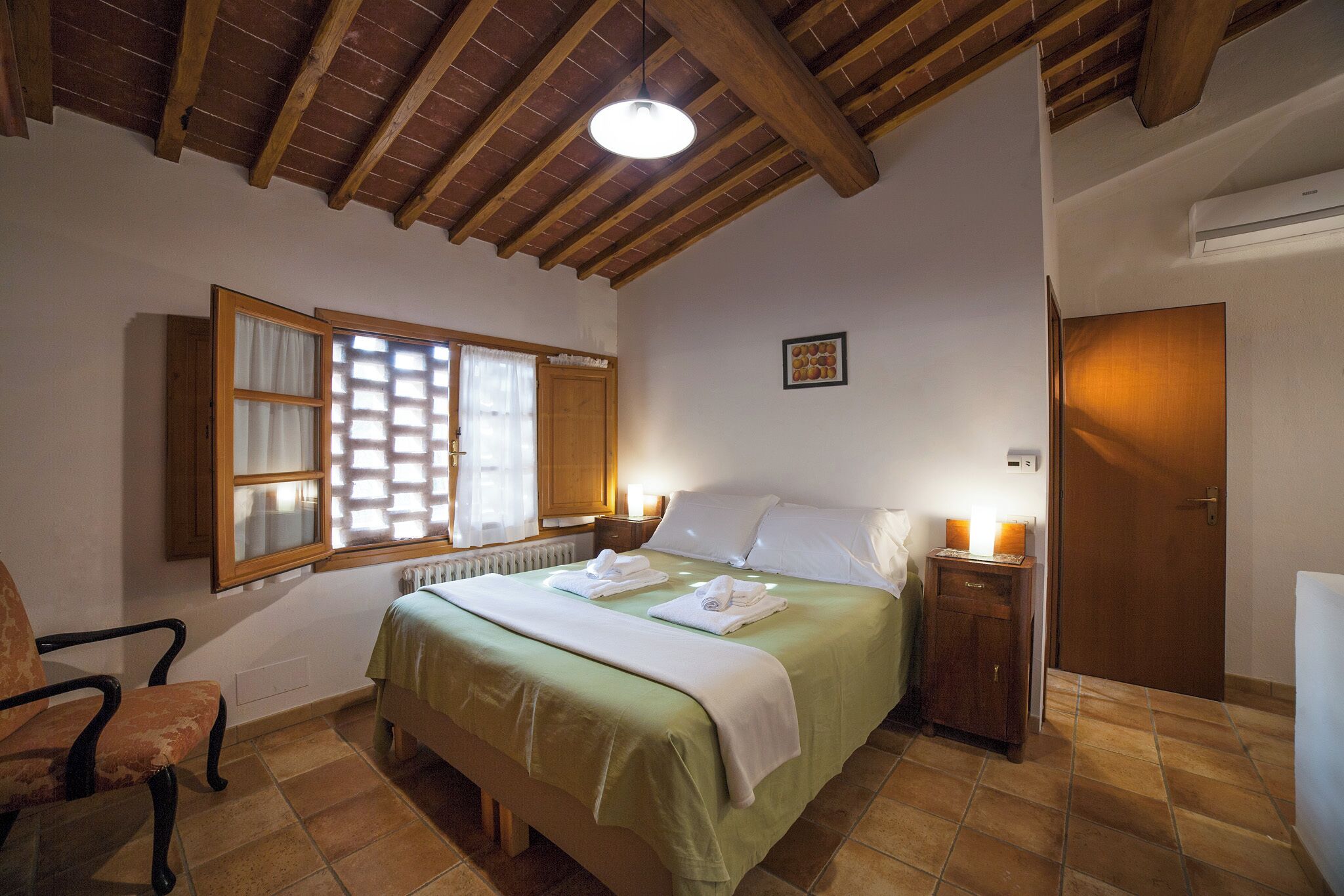 A bedroom with a bed, a chair, a window with blinds, a radiator, and a door.