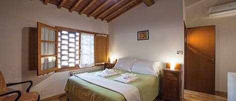 A bedroom with a bed, a chair, a window with blinds, a radiator, and a door.