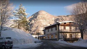 A building with a restaurant sign, a snow-covered street, and a mountain in the background. - Albergo Ristorante La Villa (Abetone Cutigliano)