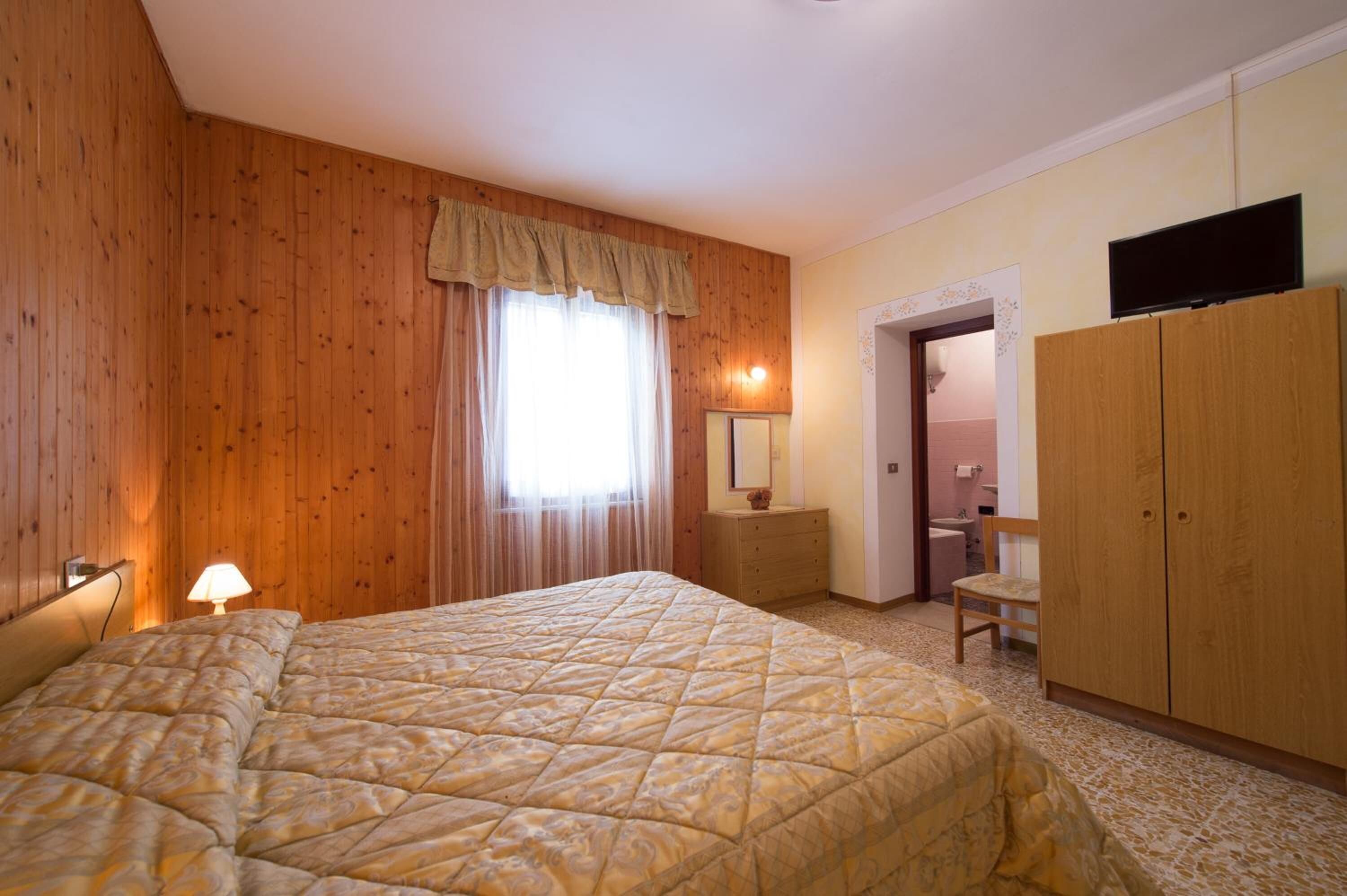 Una camera da letto con un letto grande, pareti in legno, un armadio, una scrivania e un televisore.