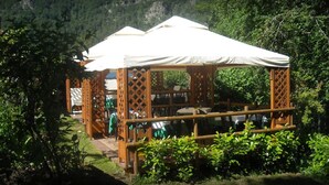 A wooden gazebo with a white canopy, surrounded by greenery and a mountainous backdrop. - Albergo Ristorante La Villa (Abetone Cutigliano)