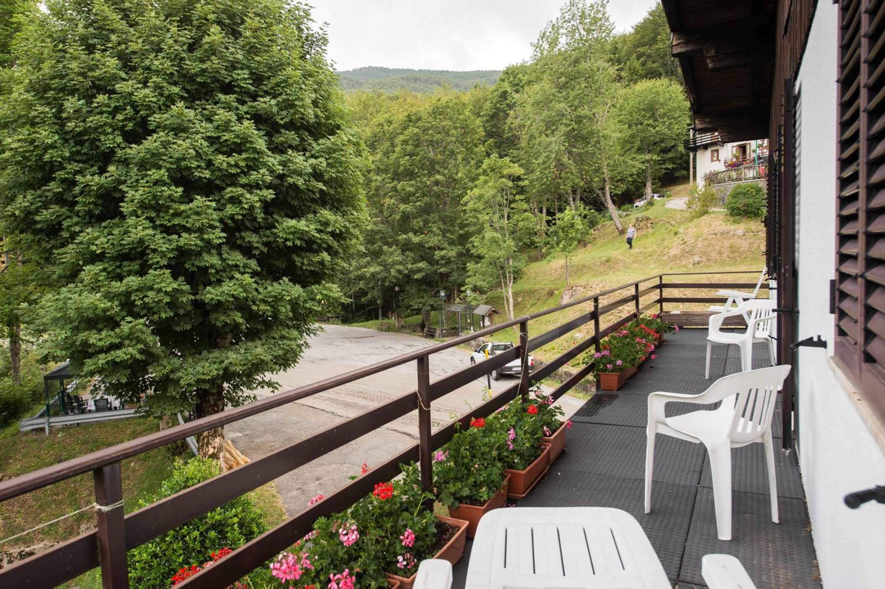 Un balcon avec des chaises en plastique blanches, des plantes en pot et une vue sur une zone boisée.