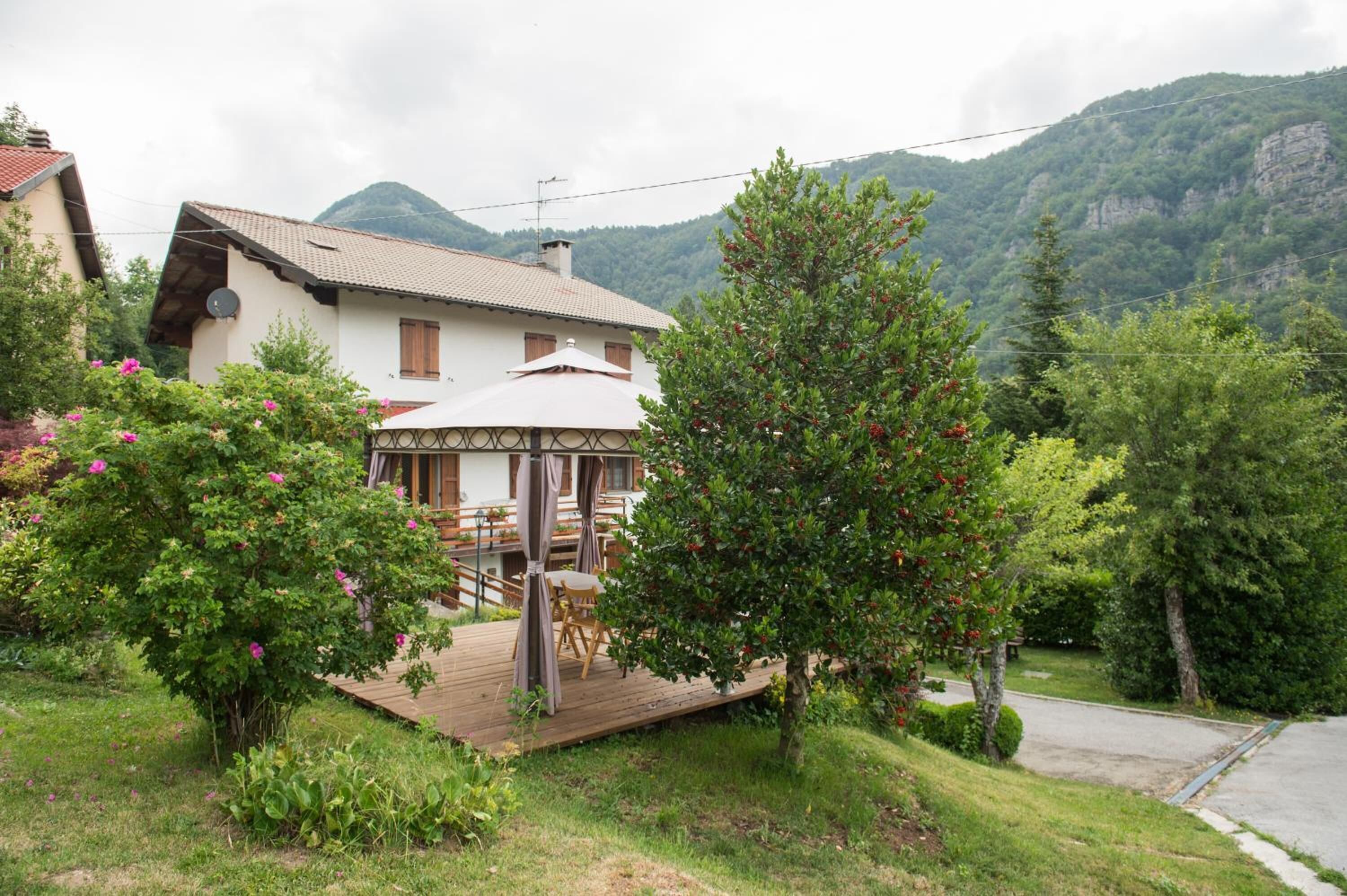 Una casa con una terrazza in legno, un'area salotto coperta e montagne sullo sfondo.
