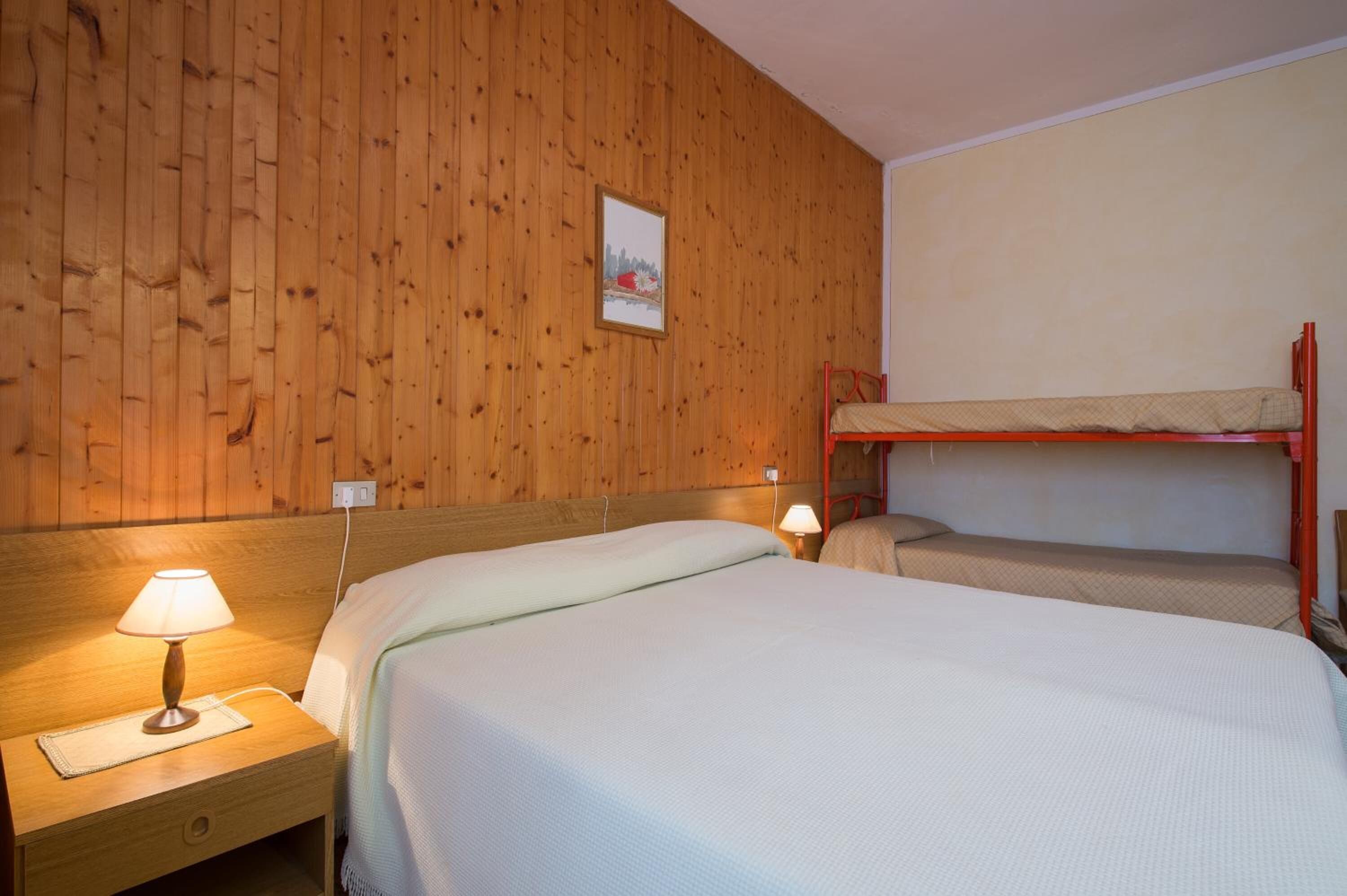 Une pièce aux murs recouverts de lambris en bois, avec un lit superposé, une table de chevet dotée d’une lampe et un tableau encadré accroché au mur.