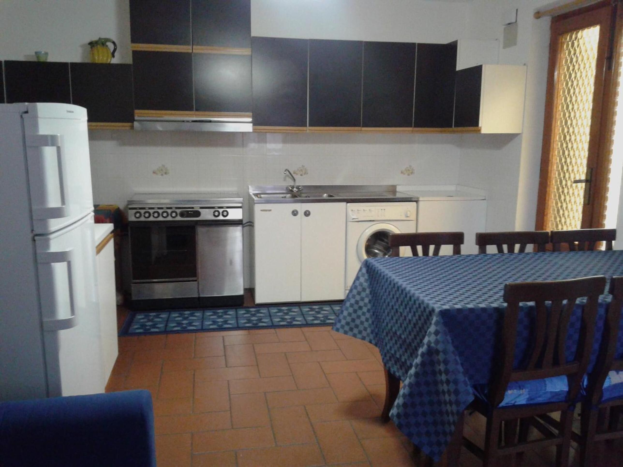 Une cuisine compacte équipée d’une cuisinière, d’un four, d’un lave-linge et d’un coin repas avec une table et des chaises.