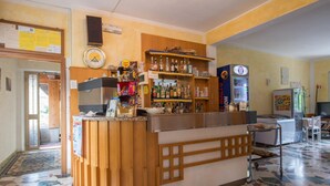 A reception area with a wooden counter, shelves with various items, a clock, and a refrigerator. - Albergo Ristorante La Villa (Abetone Cutigliano)