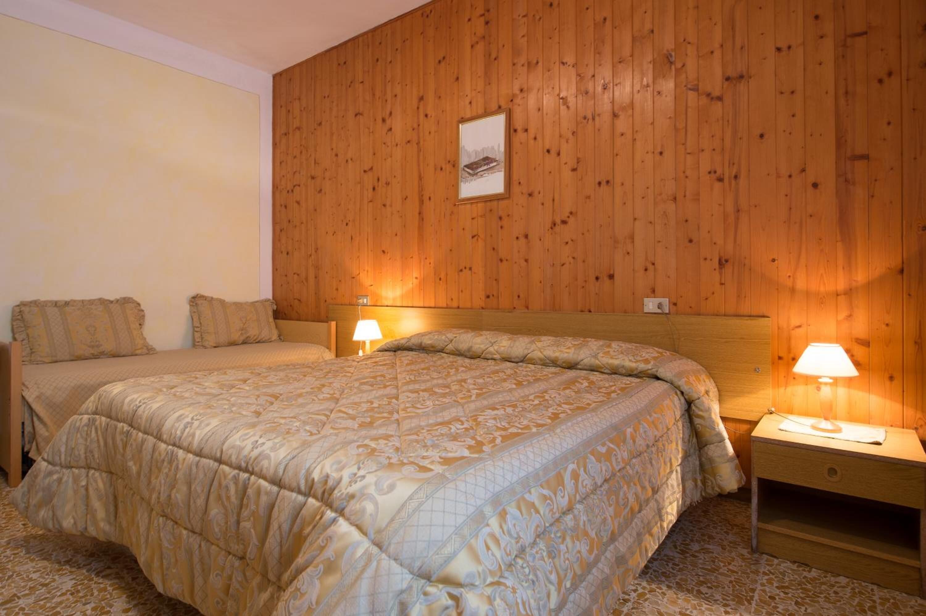 Una camera da letto con parete rivestita in legno, un letto grande con copria letto trapuntato, due lampade sui comodini e un quadro appeso alla parete.