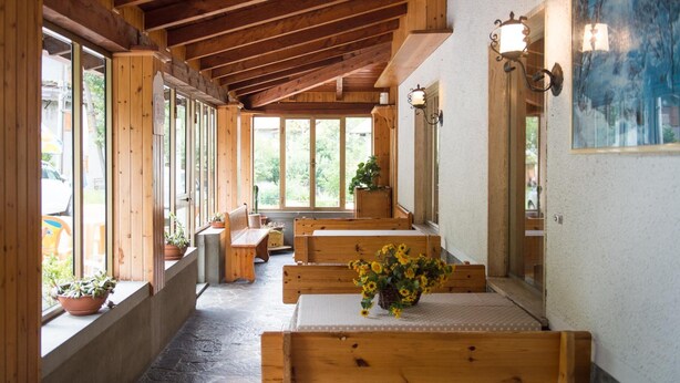 A wooden interior with benches and a table, large windows, and a stone floor. - Albergo Ristorante La Villa (Abetone Cutigliano)