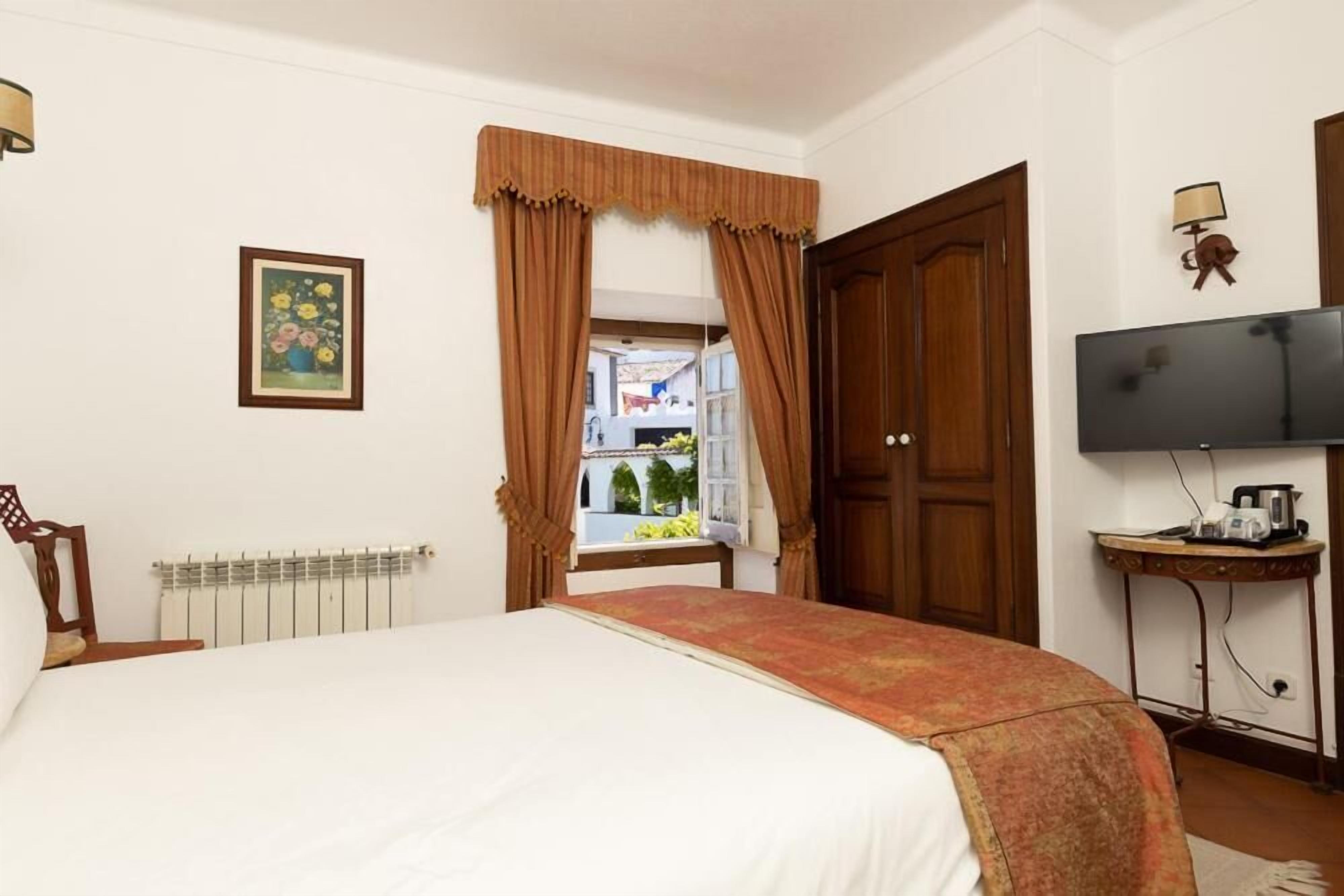 A hotel room with a bed, a radiator, a television, and a window with curtains.