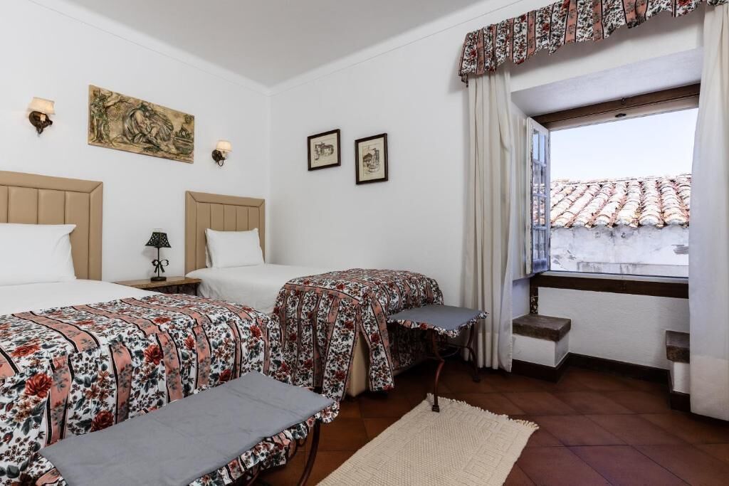 Una habitación de hotel con dos camas, una ventana con vistas y un pequeño balcón.