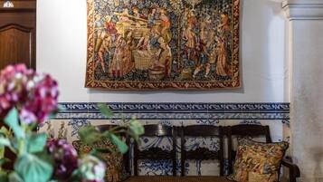 A room with a large tapestry, a wooden bench with a cushion, and a tiled wall with a blue and white pattern.