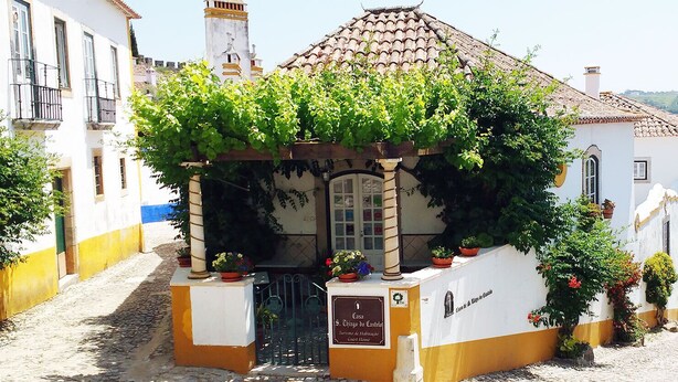 A building with a tiled roof, a sign reading "Casa do Castelo", and a small entrance with a gate. - Casa de S. Thiago do Castelo (Obidos)