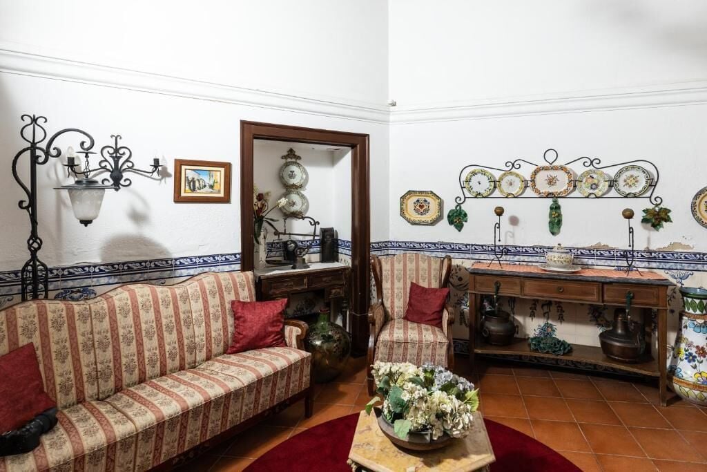 Uma sala de estar tradicional com sofá, poltronas, mesa de centro e uma parede decorativa com pratos e luminária pendente.