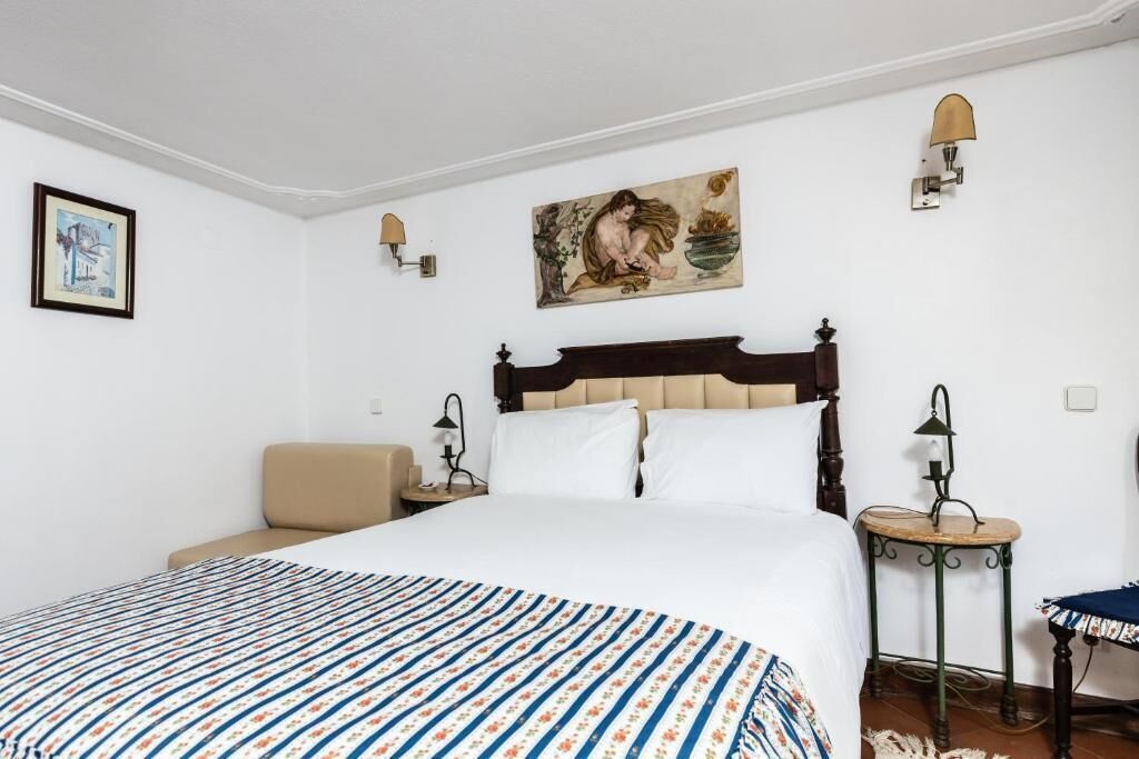 A bedroom with a large bed, a bedside table, a chair, and a wall-mounted lamp.