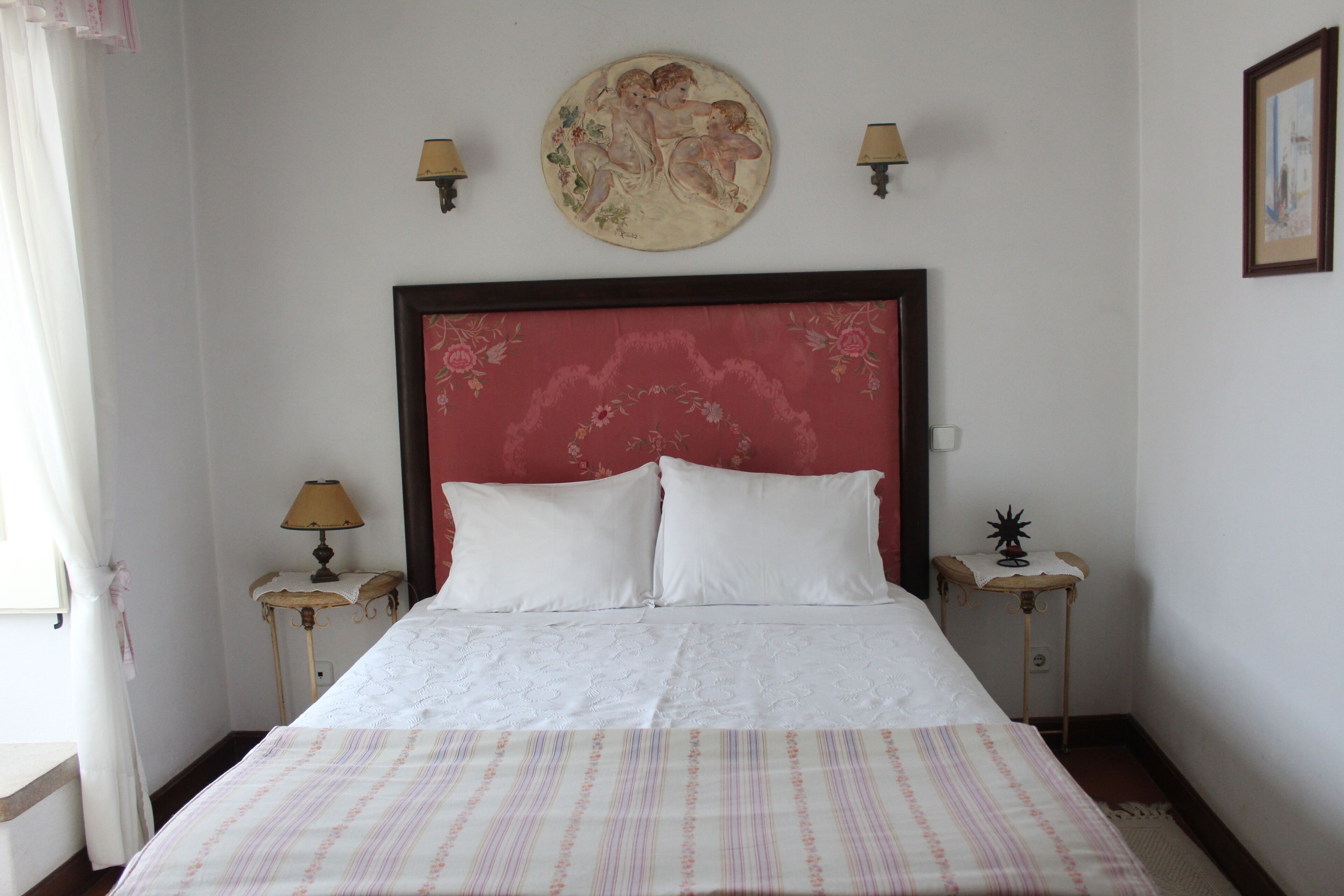 A neatly made bed with a striped bedspread, two bedside tables with lamps, a floral headboard, and a framed picture on the wall.
