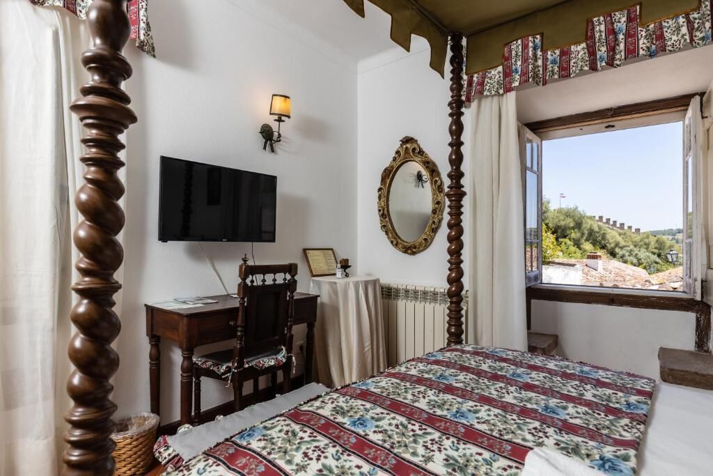 Un dormitorio con cama, escritorio, silla, televisor, espejo y ventana con vistas.