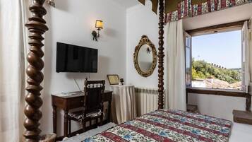 Un dormitorio con cama, escritorio, silla, televisor, espejo y ventana con vistas.