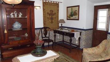 Een klassieke kamer met een houten kast, een kamerbreed tapijt met dessin, een fauteuil met bloemenprint en een tafel met lamp.