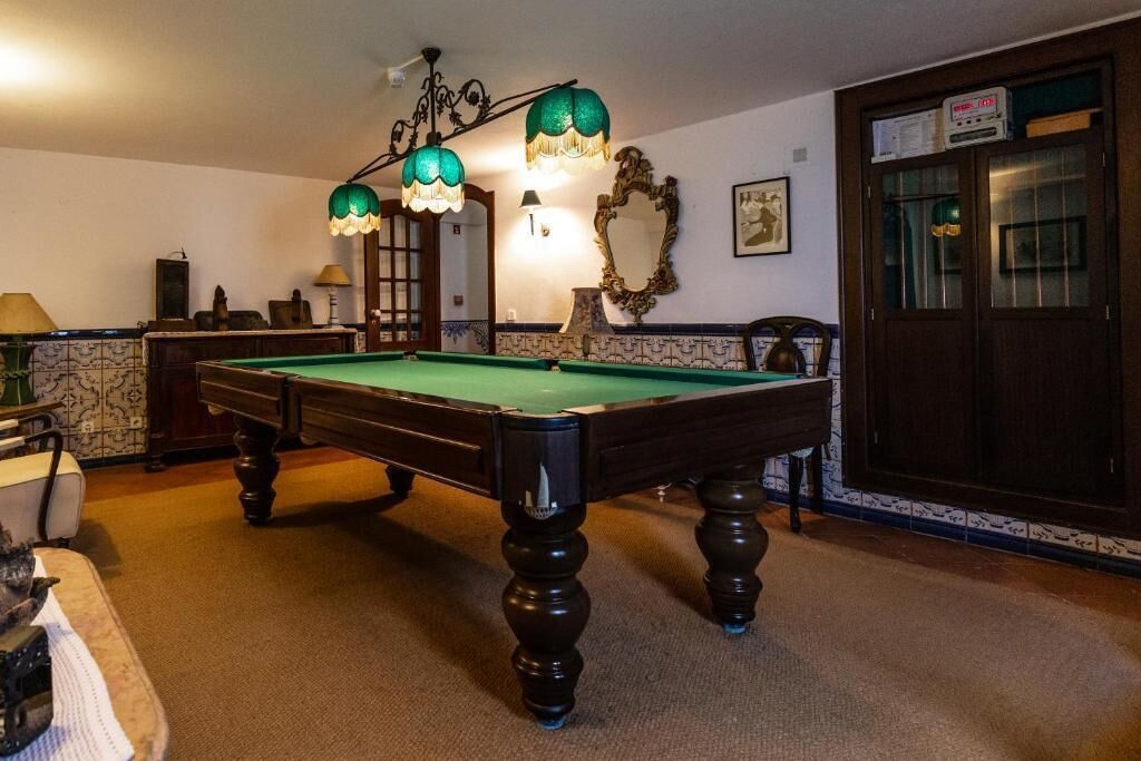A pool table in a room with a mirror, a lamp, and a cabinet.