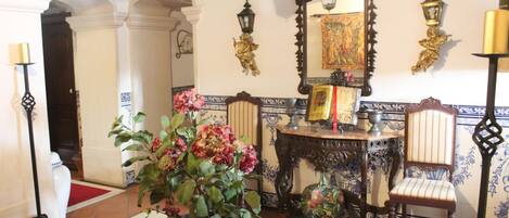 A room with a red carpet, a large potted plant, a mirror, and a table with chairs.