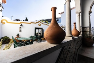 Una terraza con macetas de terracota, una mesa con sillas y un edificio blanco con un detalle amarillo decorativo.