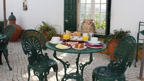 A patio with a table set for breakfast, surrounded by green metal chairs. - Casa de S. Thiago do Castelo (Obidos)