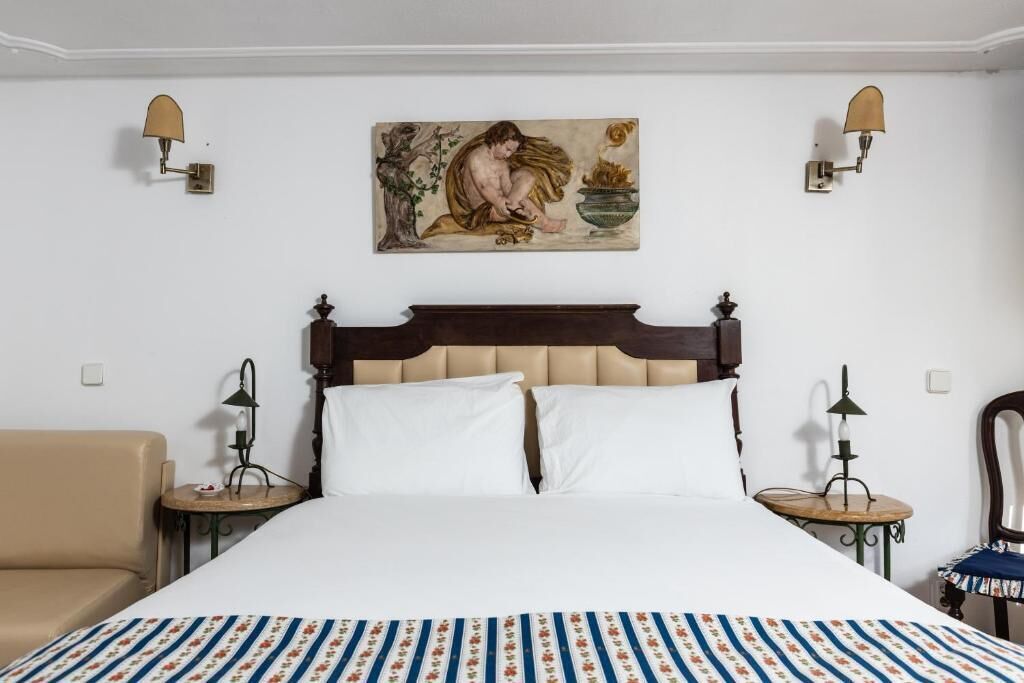 Ein Hotelzimmer mit einem großen Bett, zwei Nachttischen, einem Sessel, einem Bild an der Wand und zwei Wandleuchten.