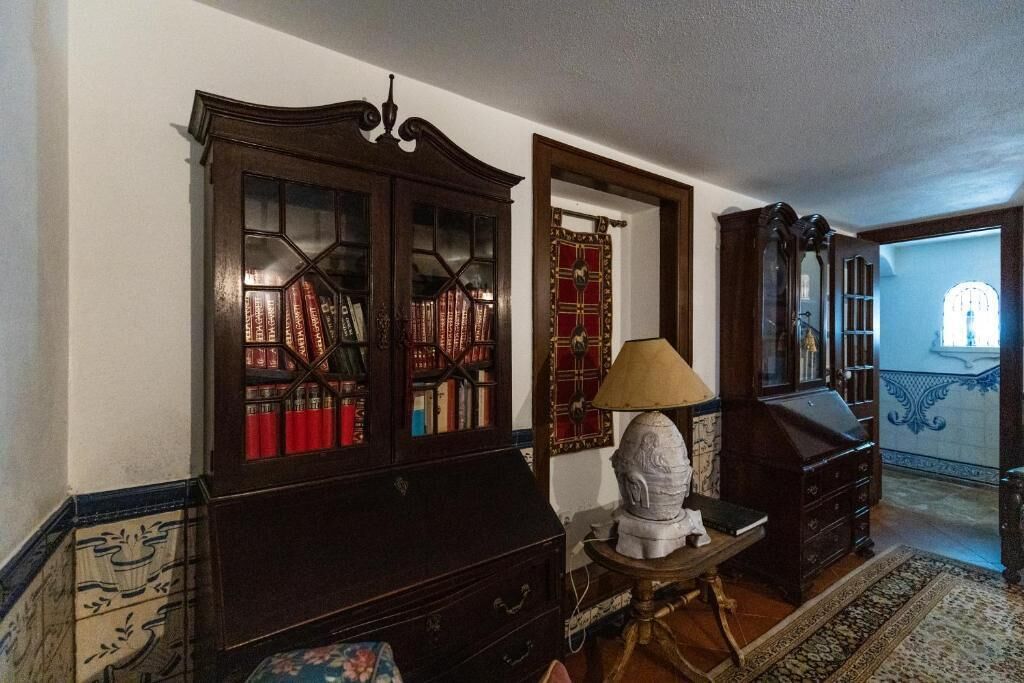 A room with a dark wooden cabinet with glass doors, a small table with a lamp, and a patterned rug.
