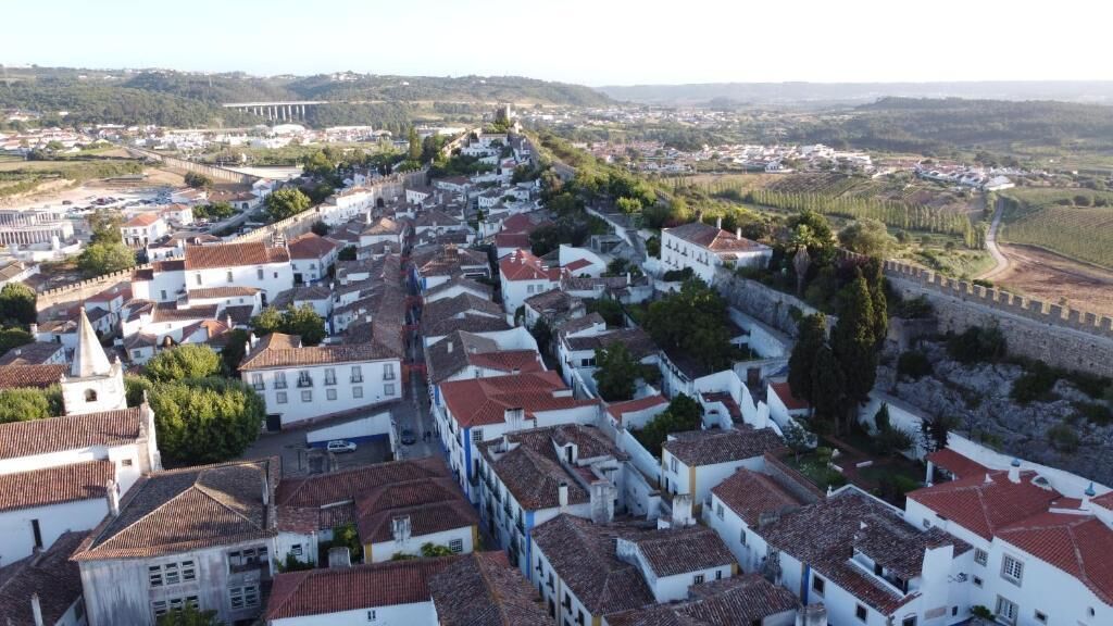 Uma cidade histórica com edifícios brancos e telhados de telha vermelha, cercada por uma muralha fortificada.