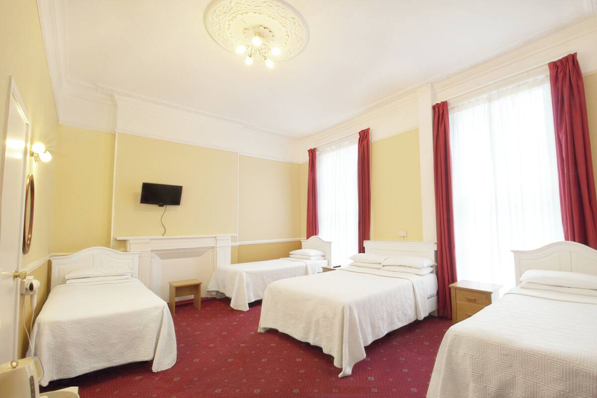 A hotel room with four single beds, a desk, a chair, and a television on the wall.