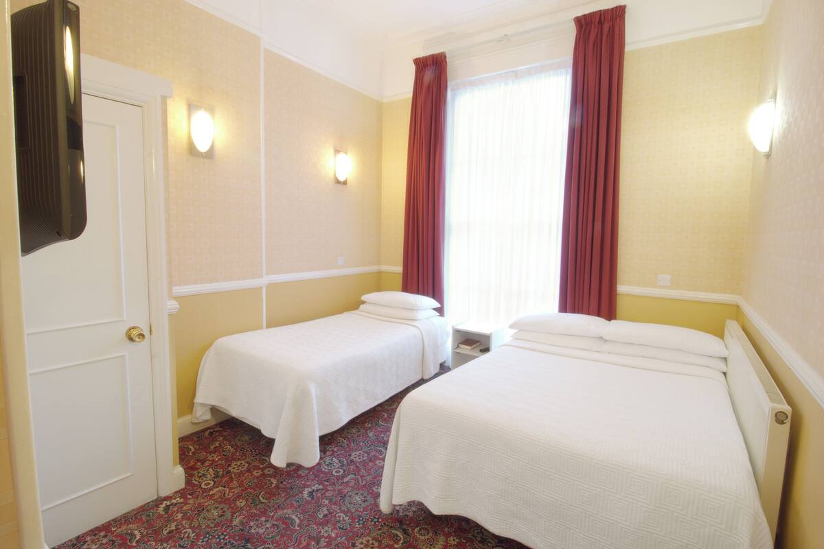 A hotel room with two single beds, a door, a mirror, and a window with curtains.
