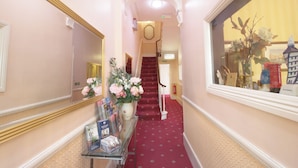 A hallway with a red carpet, a staircase, a mirror, and a vase with flowers. - Balmoral House Hotel (London)