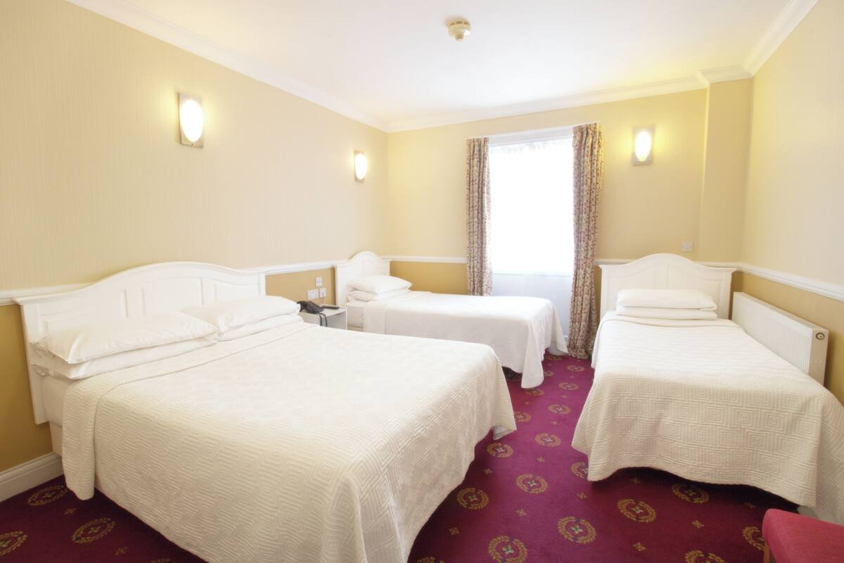 A hotel room with two single beds, a small table, and a chair.