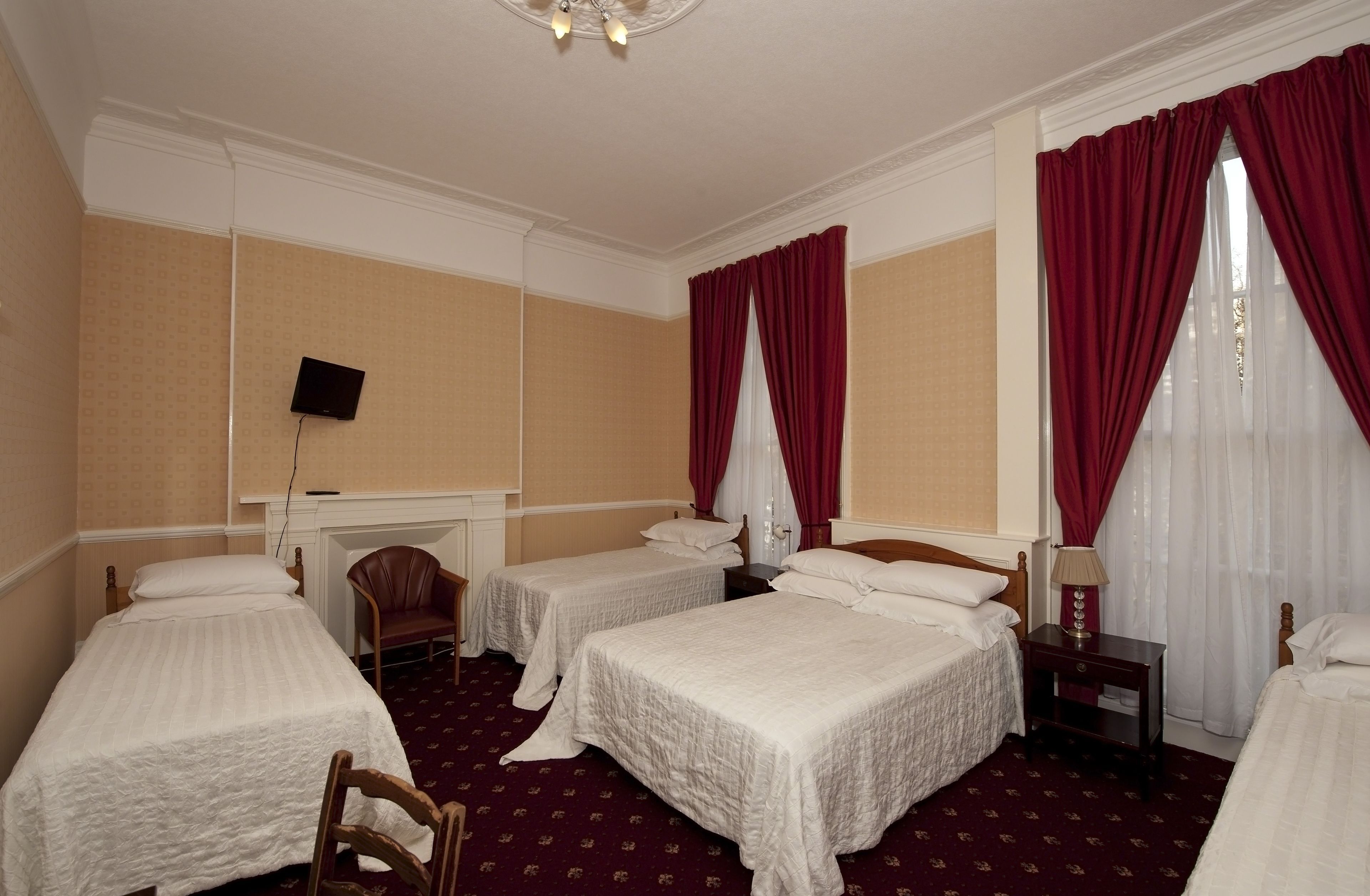 A hotel room with three single beds, a desk, a chair, a TV, and a fireplace.
