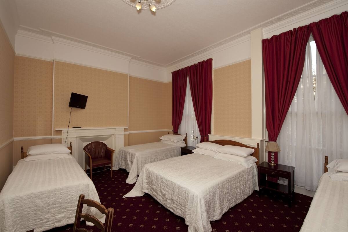 A hotel room with three single beds, a desk, a chair, a TV, and a fireplace.
