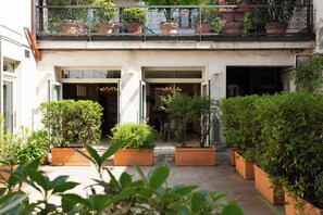 A courtyard with potted plants, a balcony with railings, and a building entrance. - La Castellana (Bergamo)