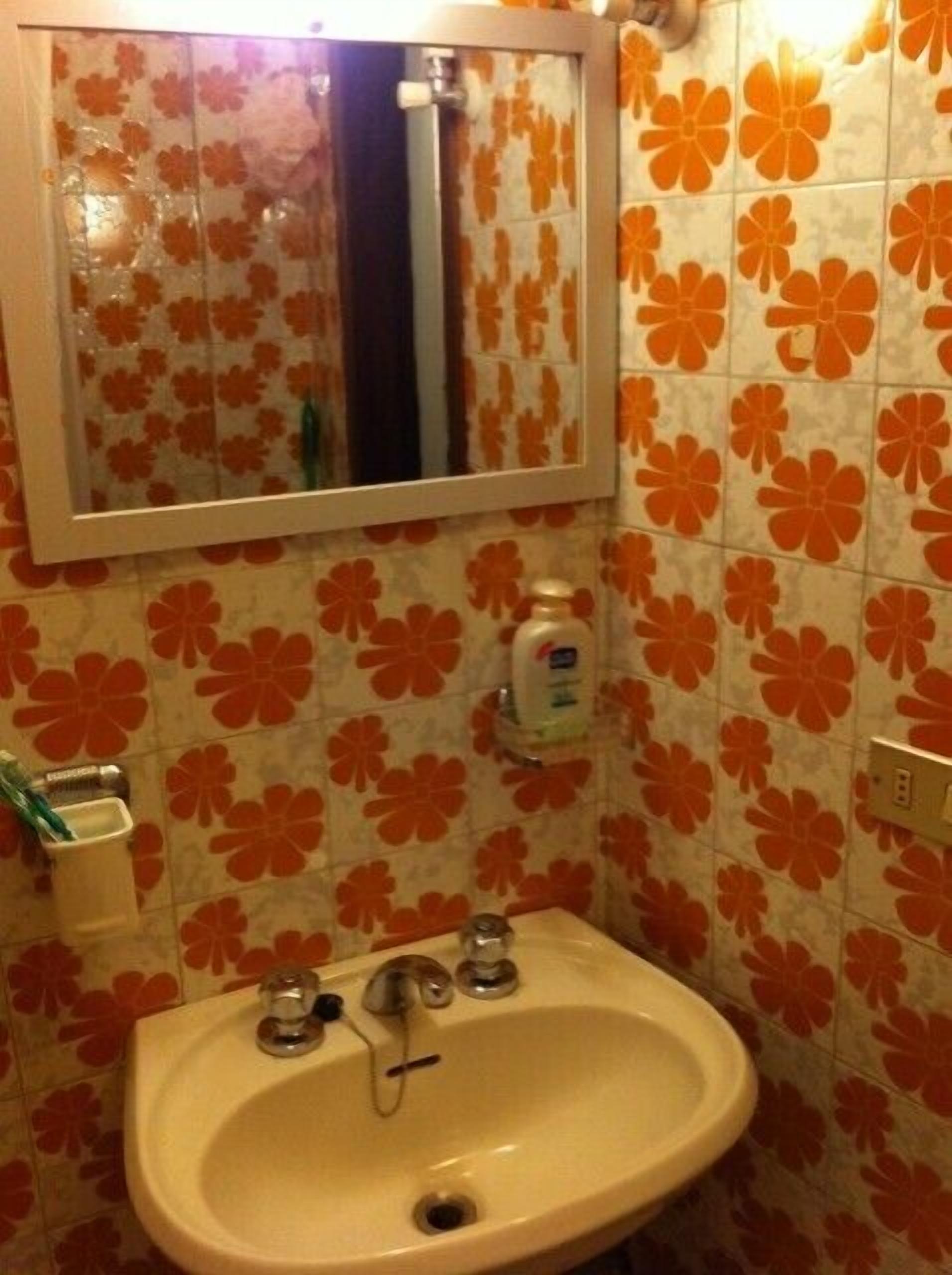 Un bagno con lavabo, specchio e piastrelle a motivi floreali.