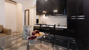 A modern kitchen with black cabinets, a glass dining table, and a bowl of fruit. - La Castellana (Bergamo)