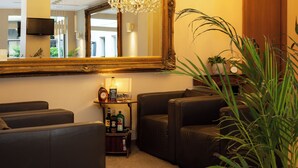 A room with a large mirror, a chandelier, leather sofas, a small table with bottles, and a potted plant. - La Castellana (Bergamo)