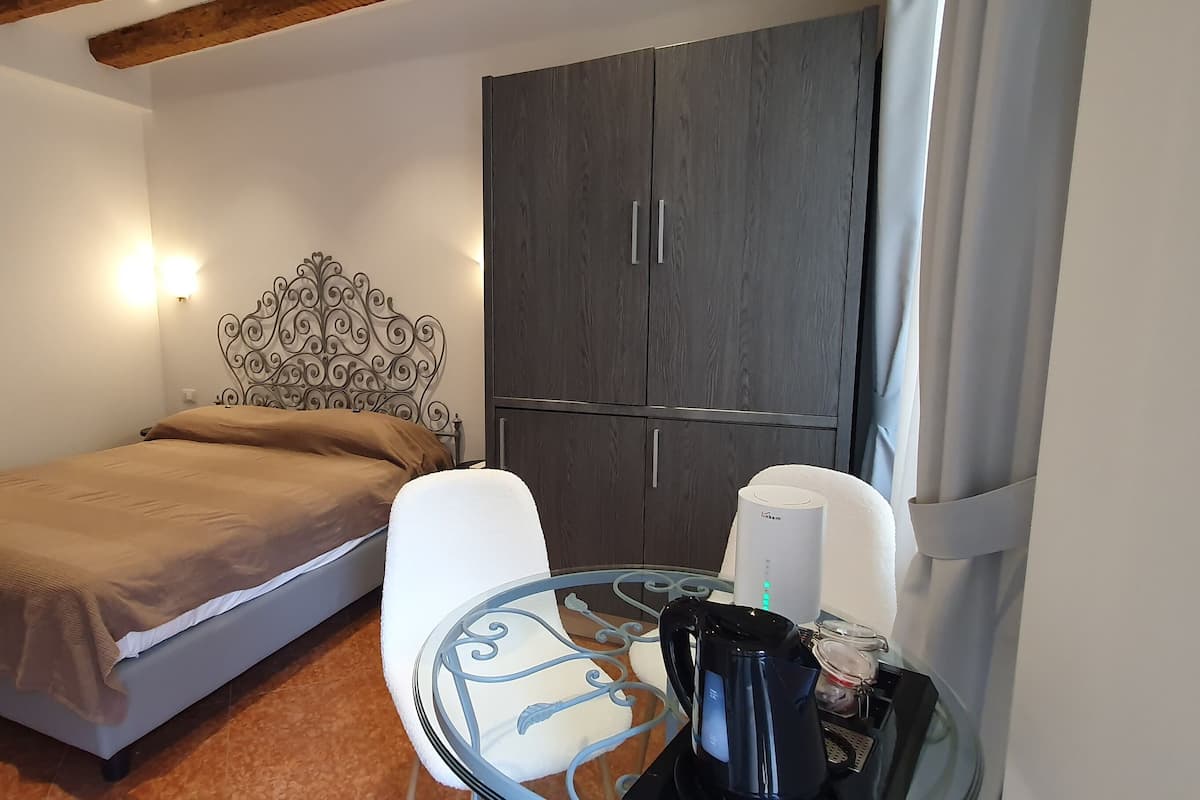 A bedroom with a bed, a wardrobe, a table with a kettle, and a lamp.