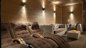 A spa room with wooden panel walls, a massage chair, a sofa, and a small table with a candle.