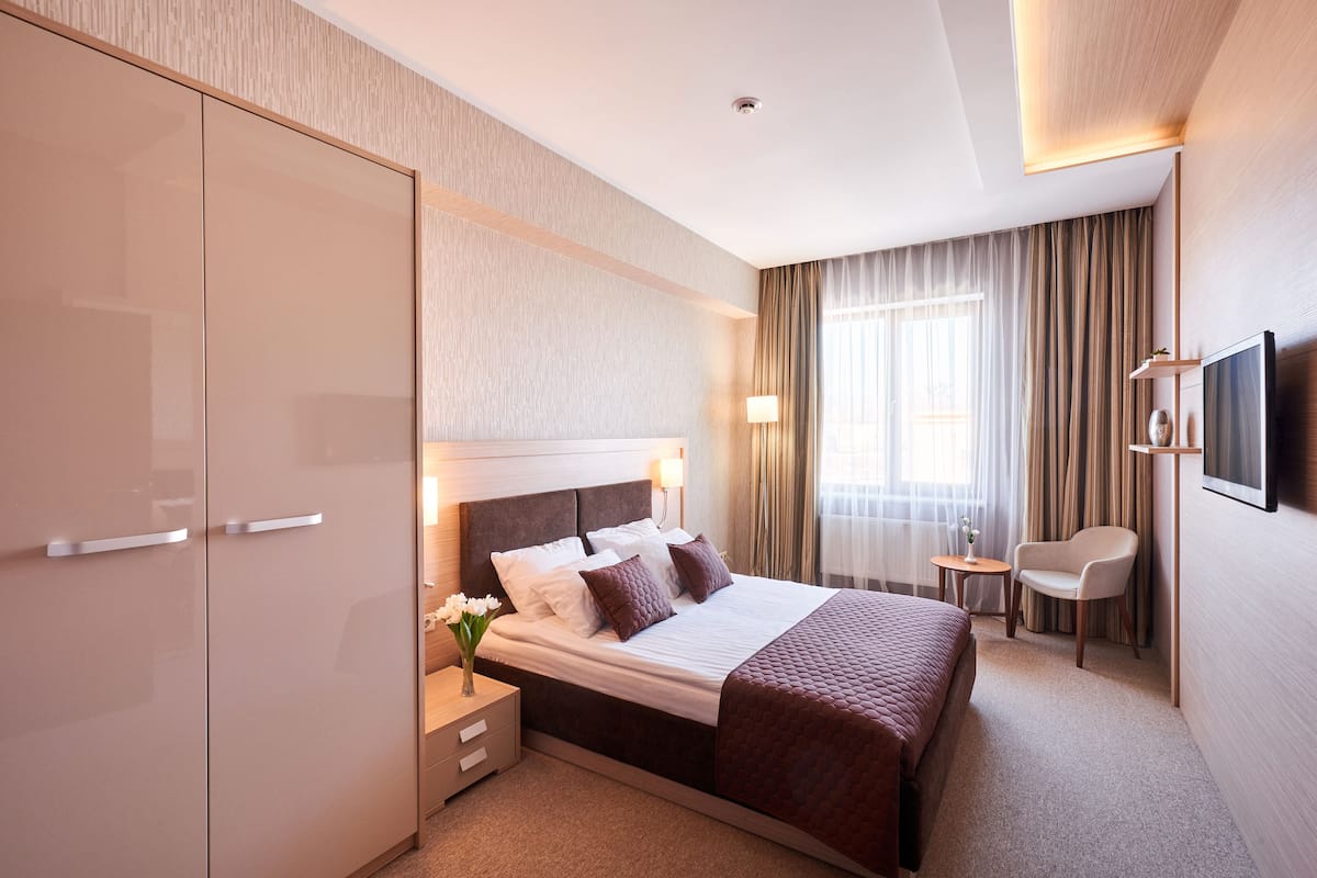 A hotel room with a large bed, a nightstand with a vase of flowers, a chair, and a TV mounted on the wall.