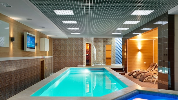 A modern indoor swimming pool with a wooden deck and lounge chairs.