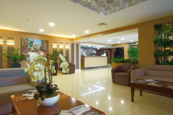 Un hall de hotel con mostrador de recepción, zonas de estar y una araña.